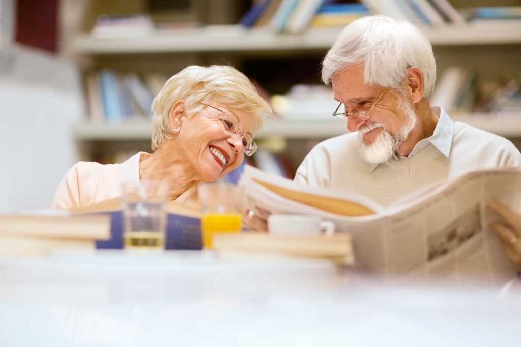 Senior couple smiling at each other while reading a newspaper