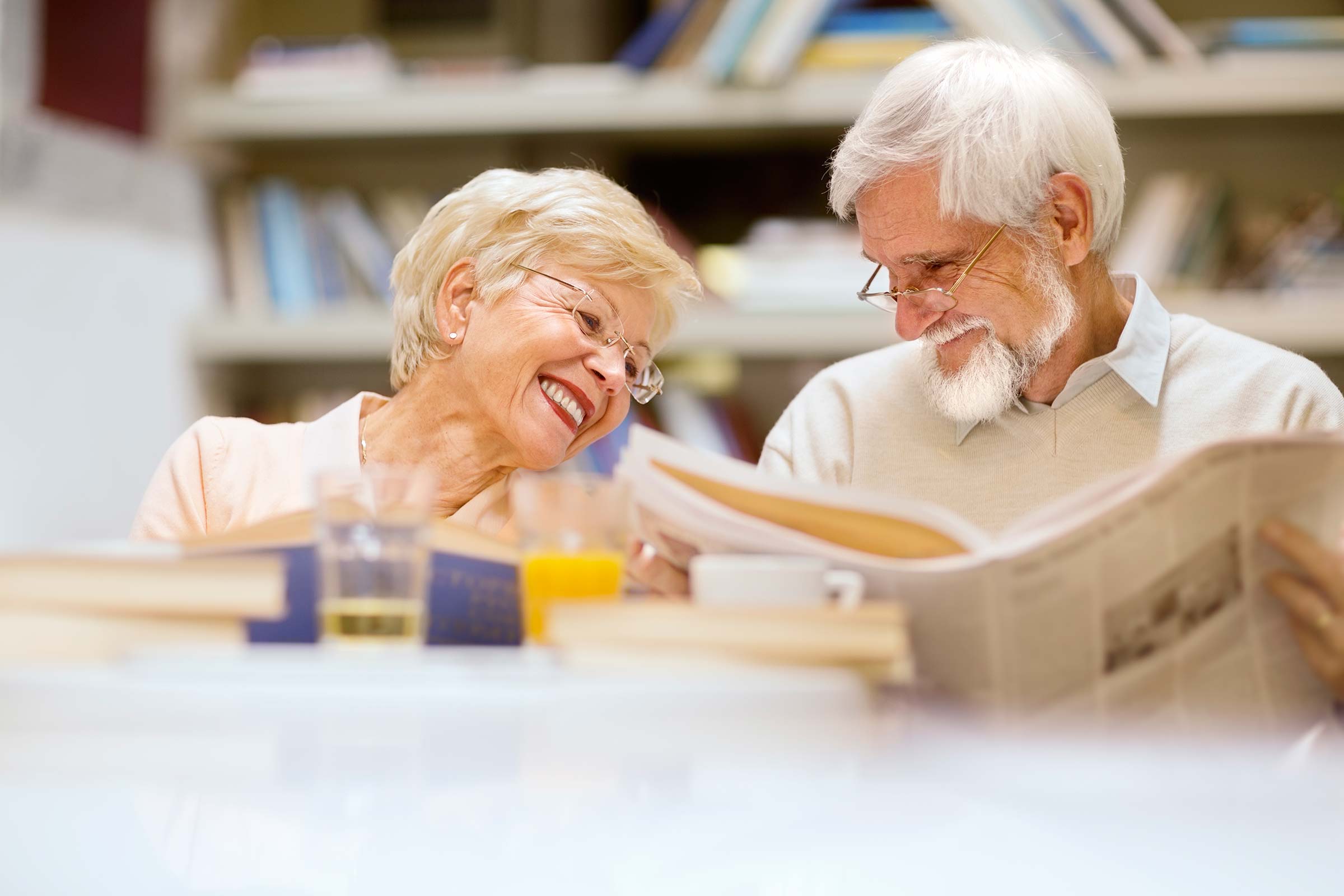 Senior couple smiling at each other while reading a newspaper