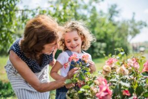 Senior woman teaching a young girl how to plant flowers in a vibrant outdoor garden.
