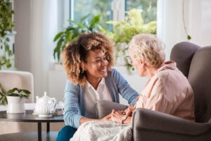 Caregiver warmly chatting with an elderly woman seated comfortably in a bright living space.