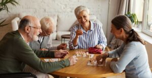 Group of senior residents gathered around a wooden table playing bingo together at Park Place of Elmhurst, smiling and enjoying social time.