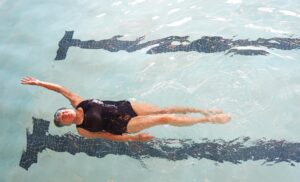 a senior woman doing a backstroke in an indoor pool