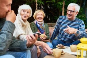 Four seniors sitting outside on their deck enjoying coffee and snacks while talking