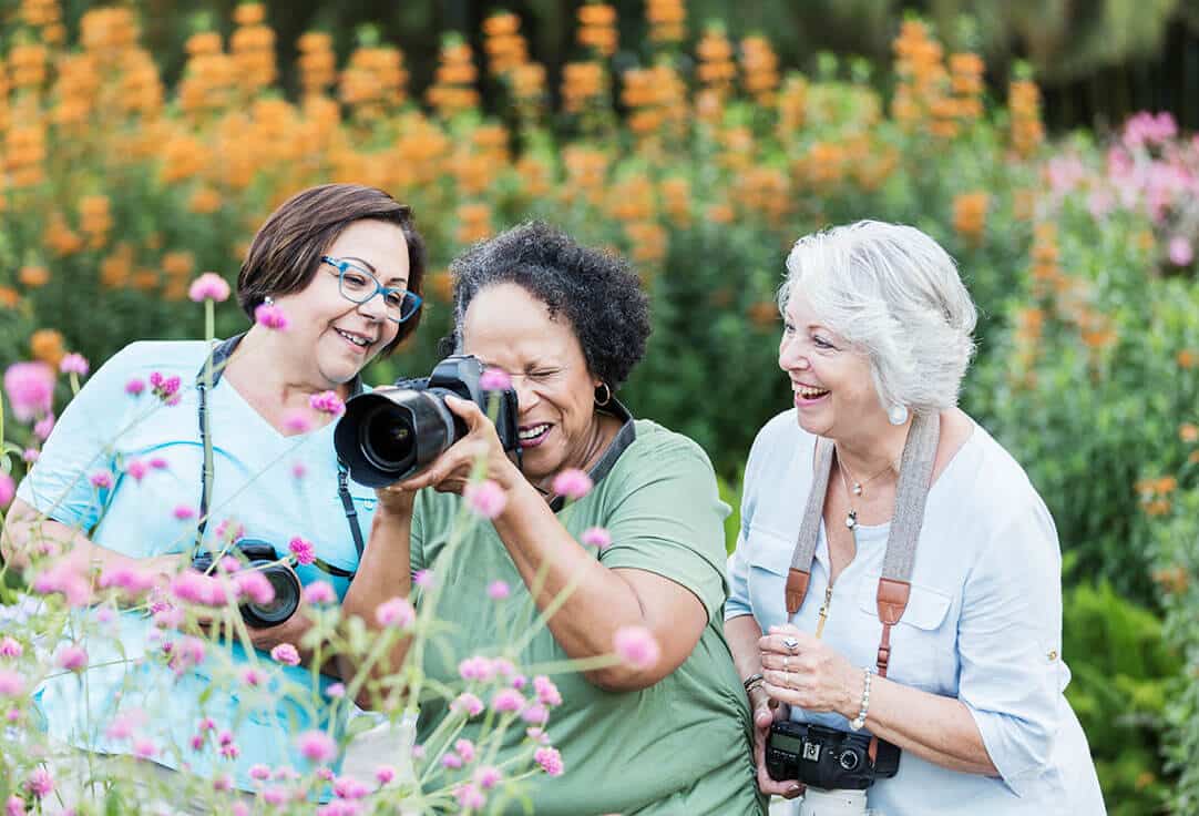 Three women with cameras taking pictures in a garden full of beautiful flowers.