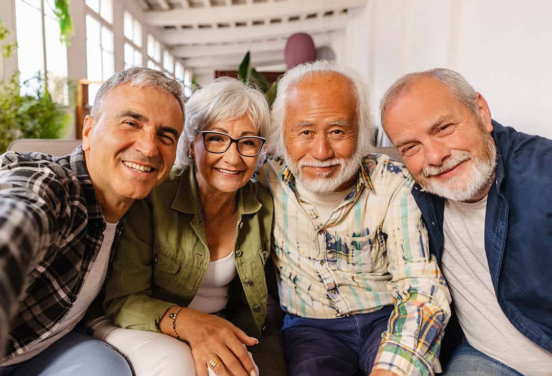 Three older men and a woman sitting on a couch together smiling for a selfie.
